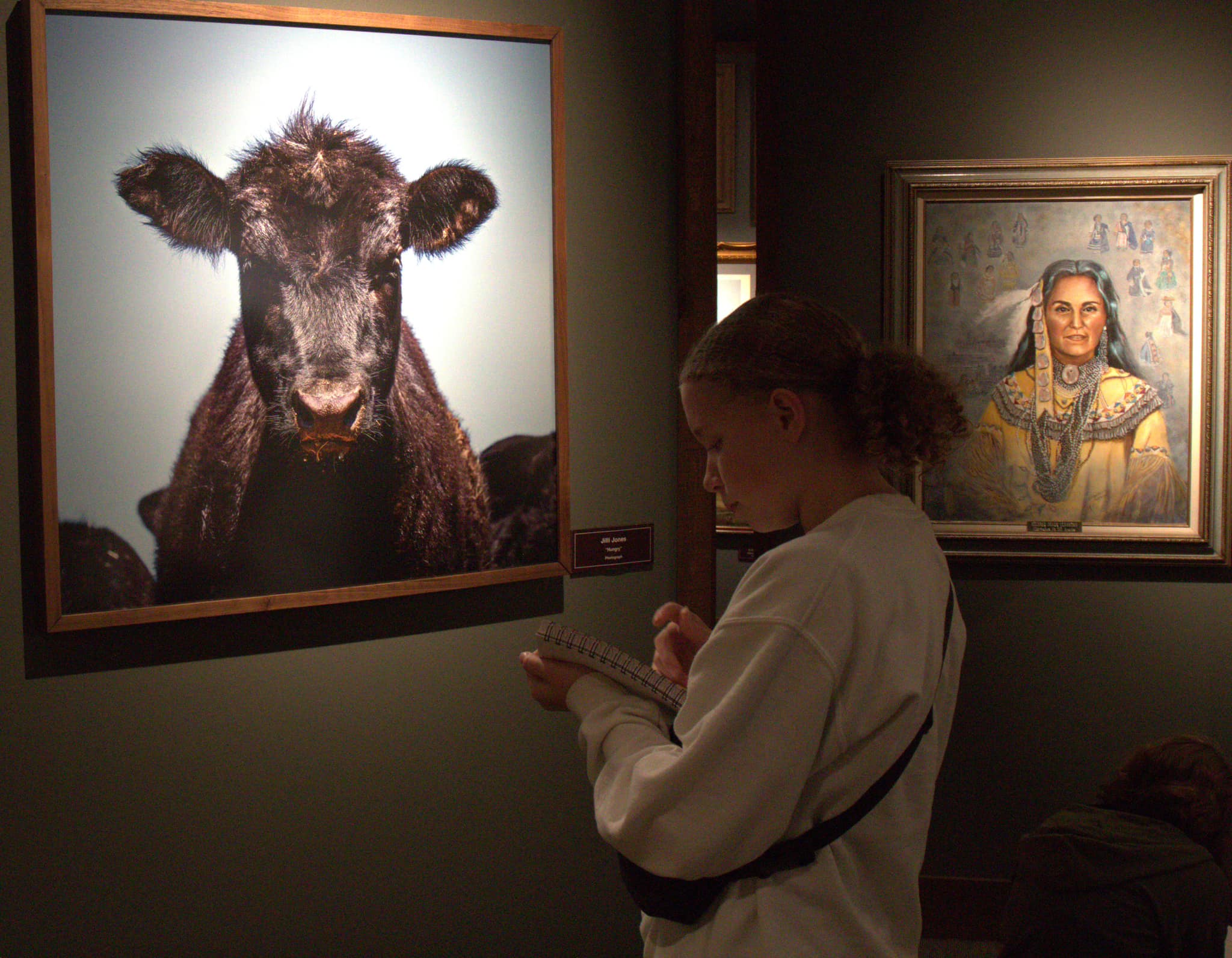A teen girl taking notes by a painting of a cow in the Garis Gallery