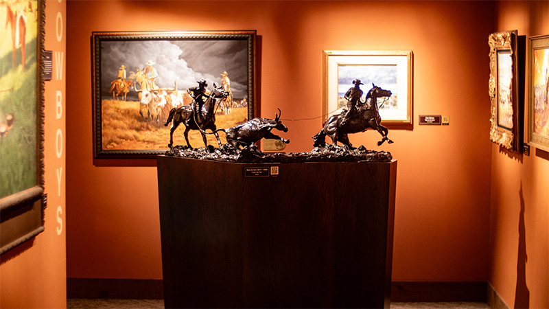Bronze statue in an orange walled gallery with many paintings on the walls.